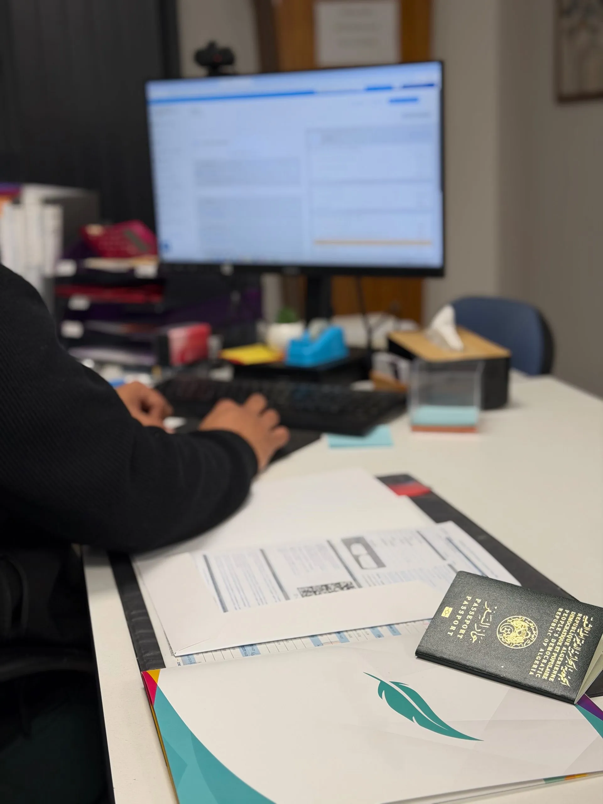 Vue de trois-quarts dos d'un conseiller travaillant sur ordinateur à son bureau avec passeport et documents administratifs