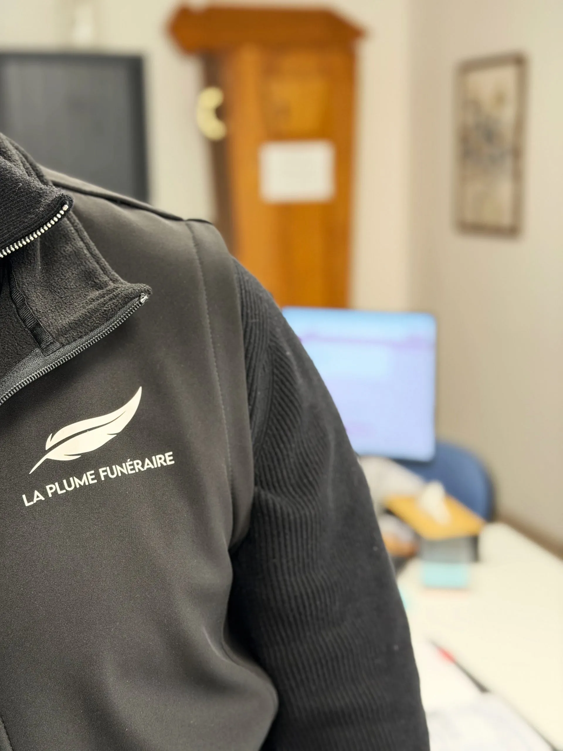 Gros plan sur la veste noire d'un conseiller portant le logo La Plume Funéraire