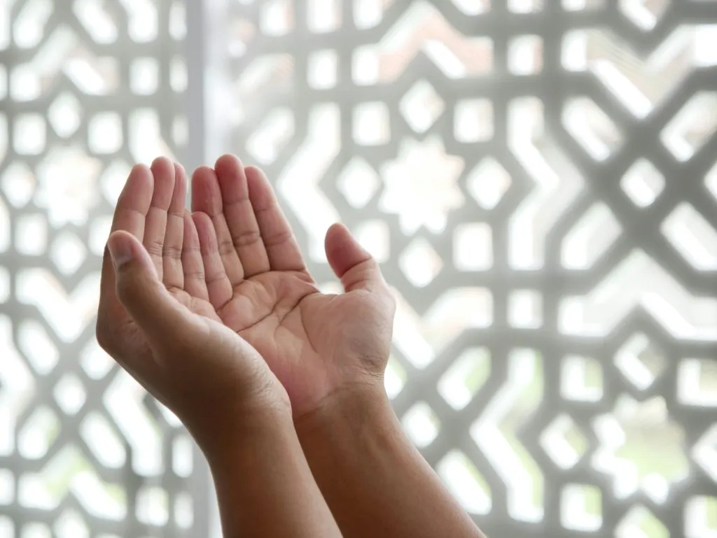 Mains ouvertes levées en geste de prière spirituelle devant un moucharabieh