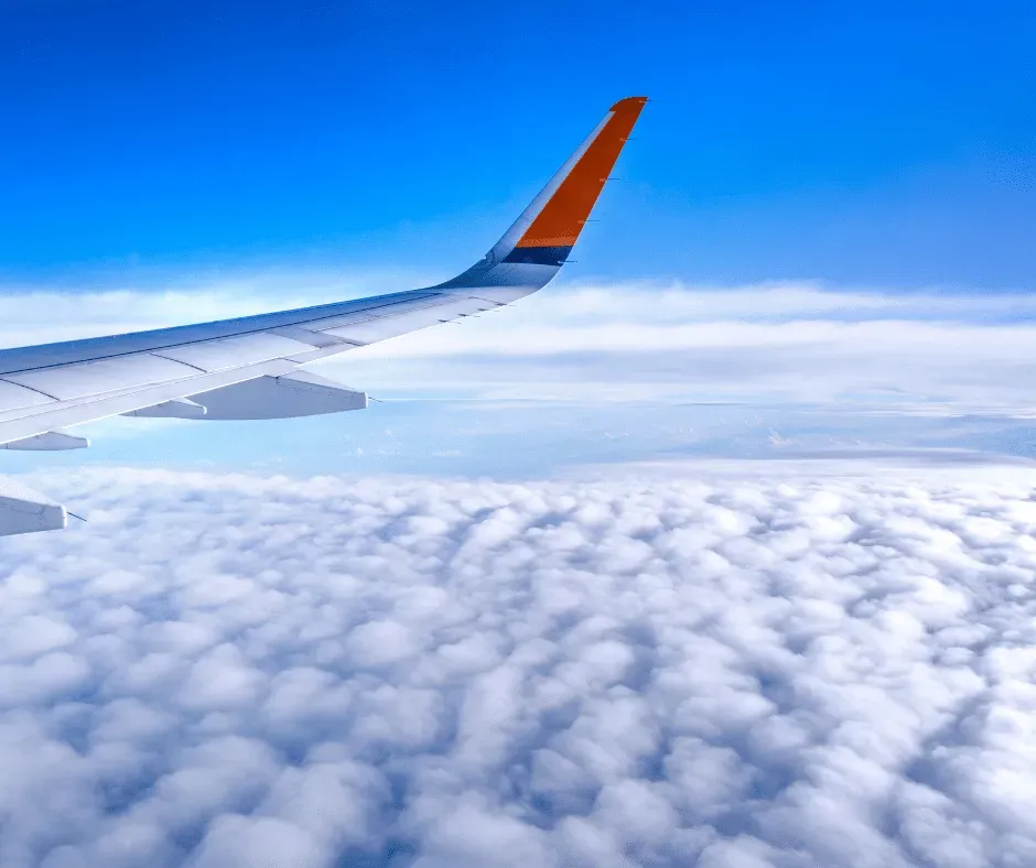 Aile d'avion de ligne volant au-dessus d'un tapis de nuages blancs sous un ciel bleu